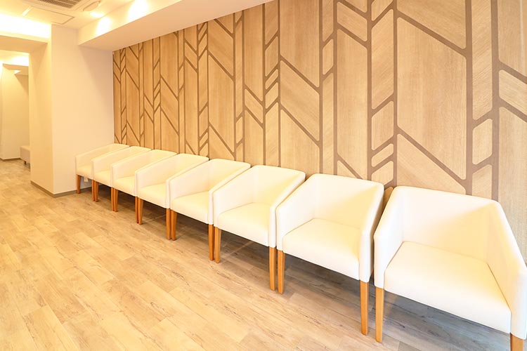 広々とした空間に、木目調の壁と落ち着いた色合いの椅子が並びます。患者様にリラックスしてお待ちいただけるよう、清潔感と居心地の良い空間をご提供します。